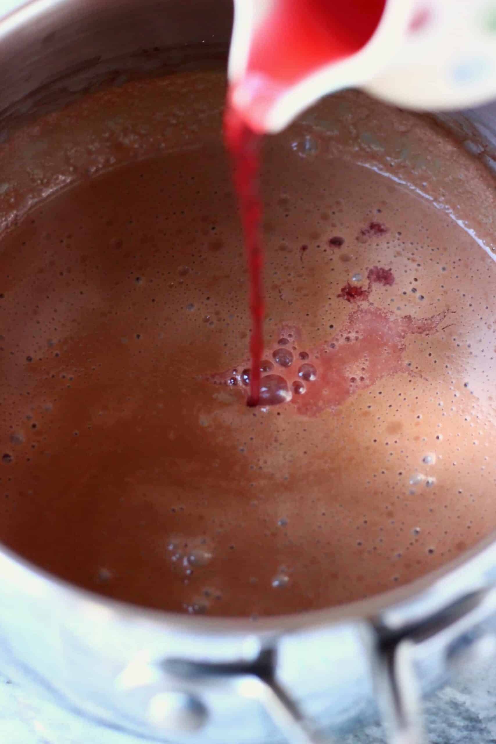 Vegan hot chocolate in a pan with red wine being poured in from a jug