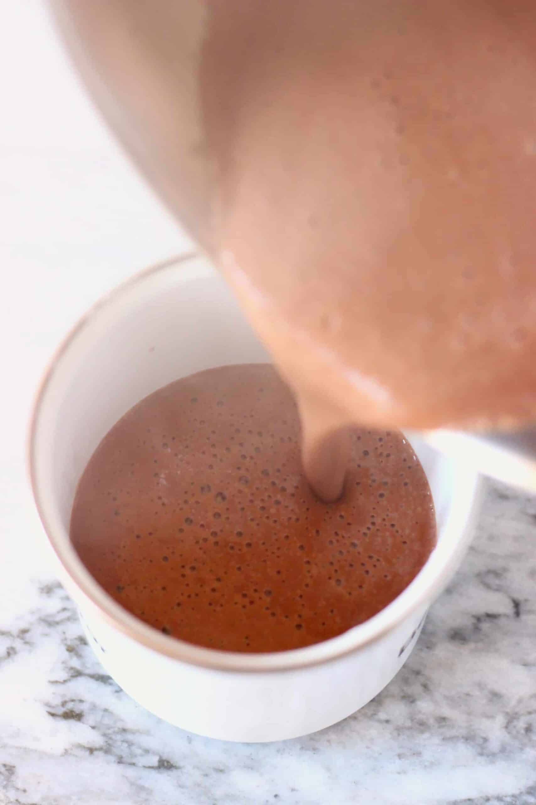 Red wine hot chocolate being poured into a mug from a pan