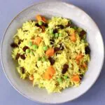 Photo of yellow rice with vegetables in a ceramic bowl against a grey background