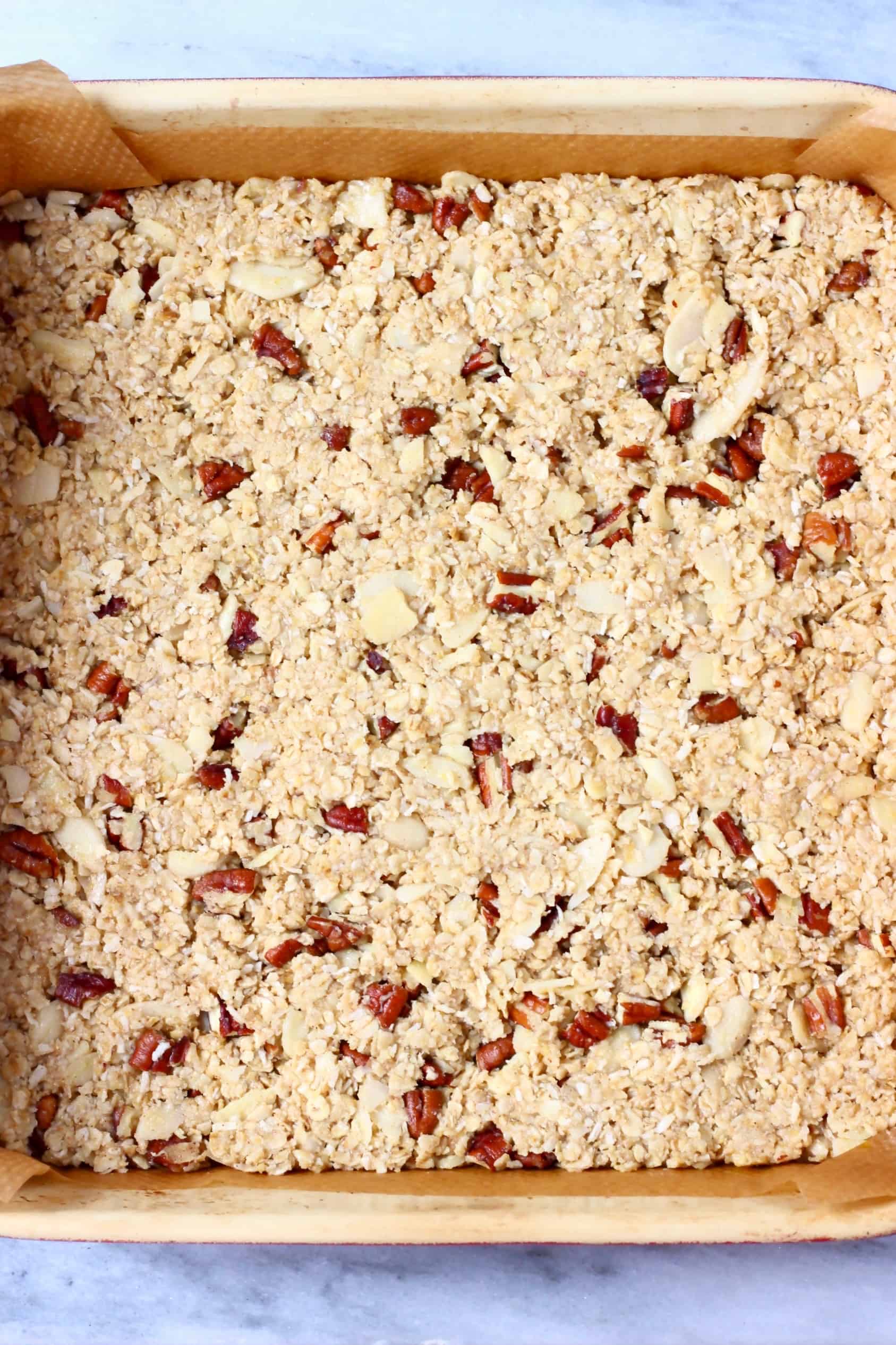 Raw vegan granola bar mixture in a square baking tin lined with baking paper