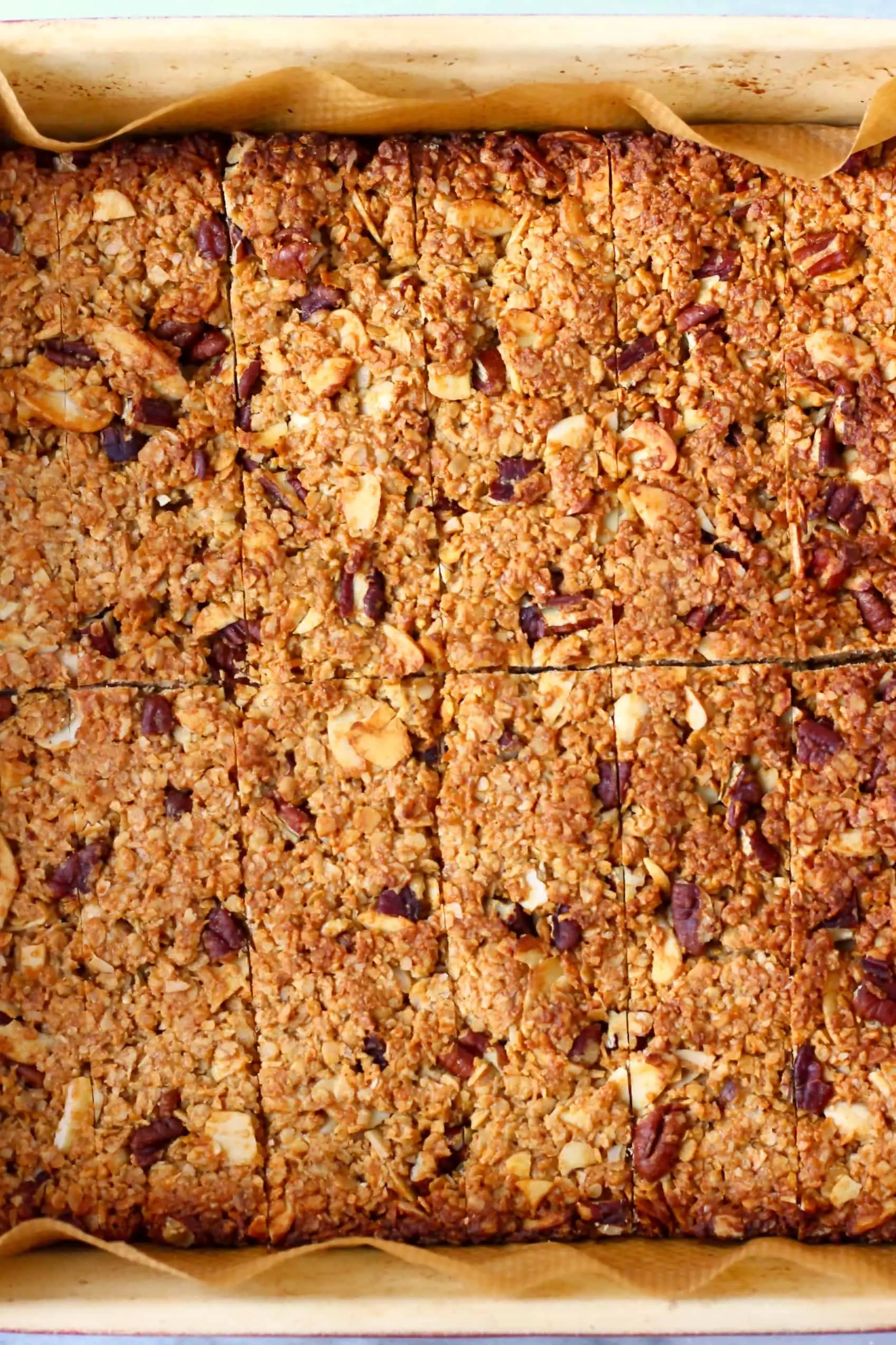 Sliced vegan granola bars in a square baking tin lined with baking paper