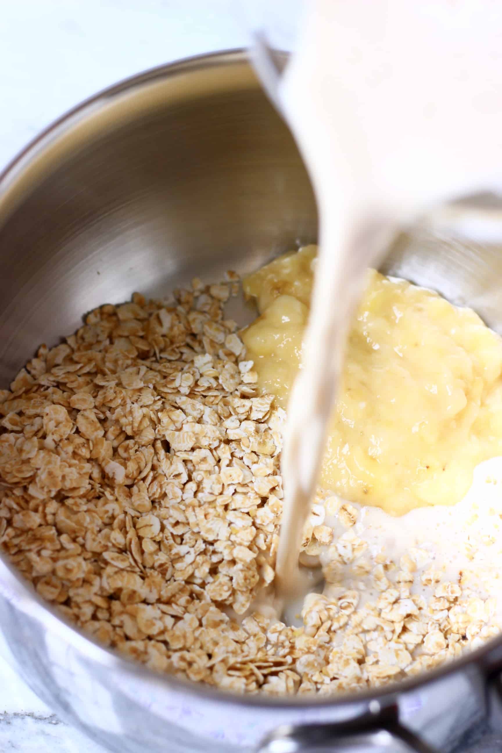 Mashed banana and oats in a pan with plant-based milk being poured into it from a jug