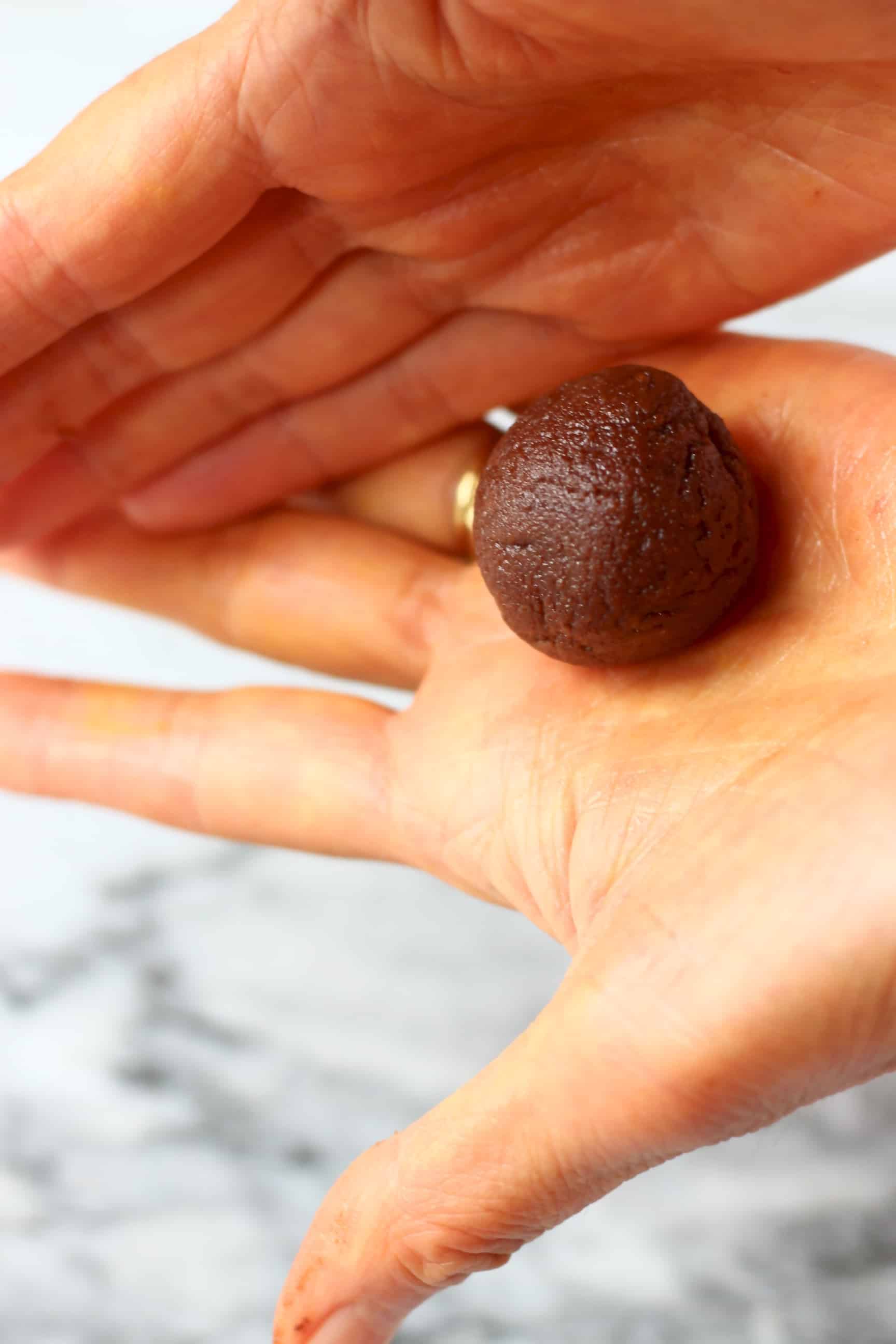 These Vegan Cashew Chocolate Truffles are the most delicious treat - they're melt-in-your-mouth silky, super creamy, and unbelievably healthy! Also gluten-free, paleo and refined sugar free. #rhiansrecipes #chocolate #vegan #glutenfree #dairyfree #paleo Two hands rolling a round vegan chocolate truffle into a ball