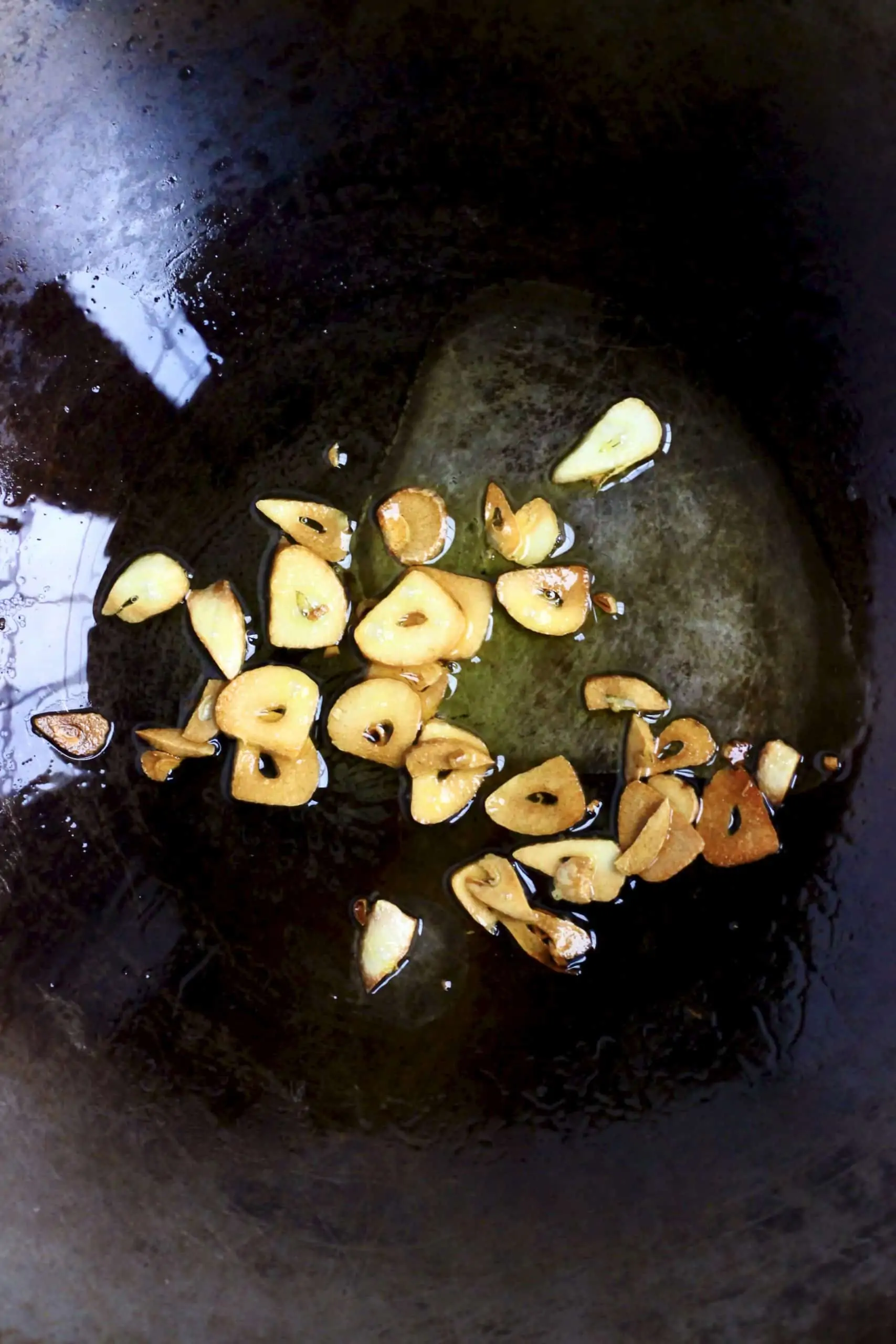 Golden brown sliced garlic being fried in a black wok
