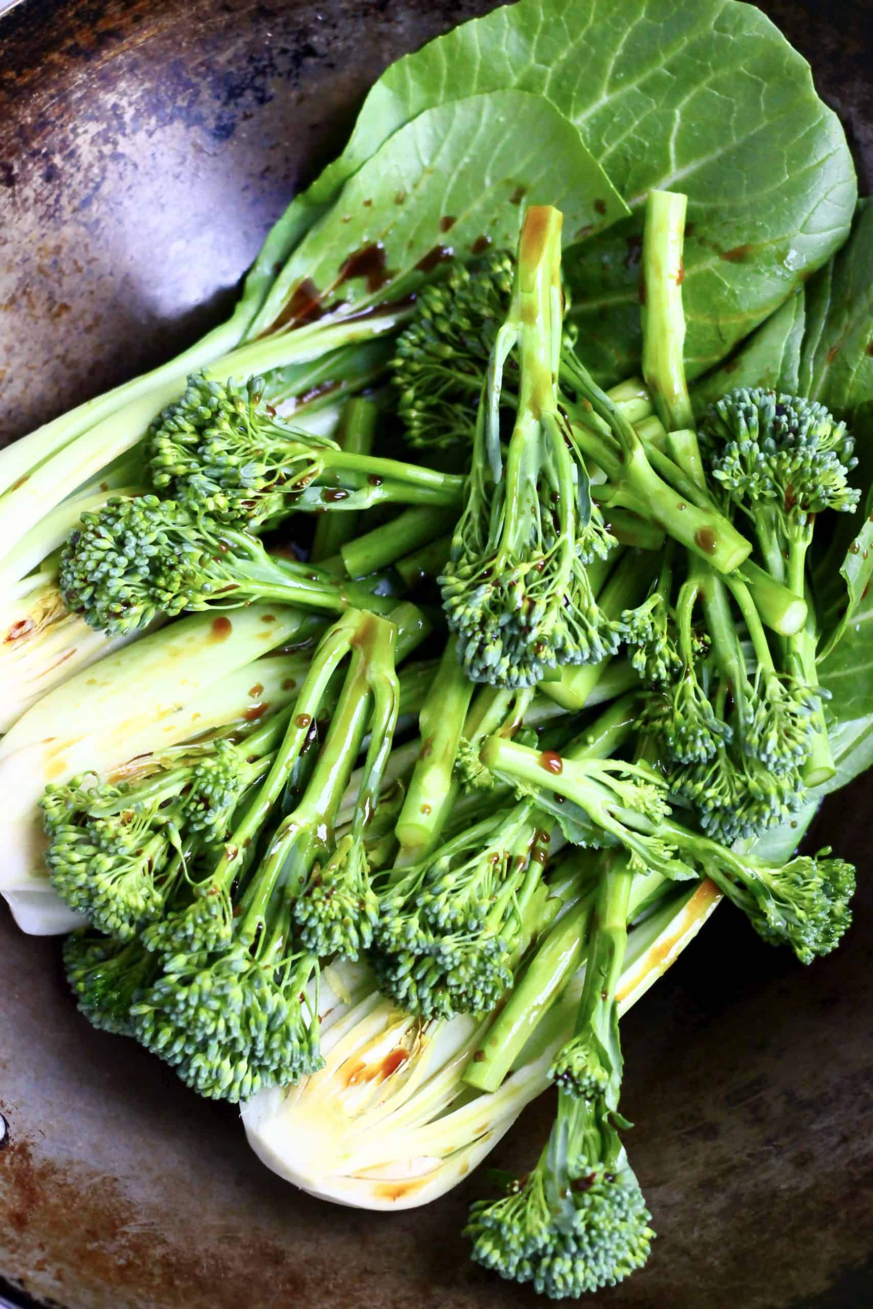 Raw tenderstem broccoli and pak choi with sauce in a black wok