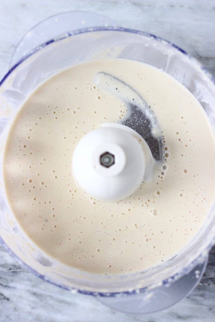 White cashew cream in a food processor against a marble background