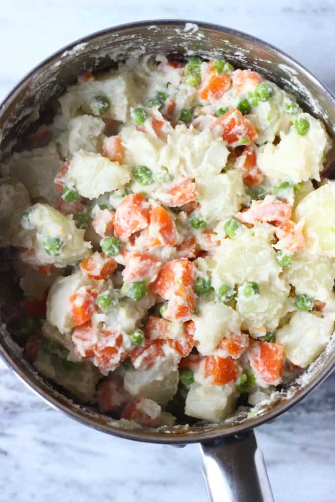 This Vegan Potato Salad is a great make-ahead side dish - it's easy to make, irresistibly creamy, and healthier than the traditional version! Made with carrots and green peas and is highly customisable. Vegetarian, dairy-free, egg-free, gluten-free, oil-free. #rhiansrecipes #vegan #potatosalad #sidedish #glutenfree #dairyfree Potato salad with carrots, green peas and mayonnaise in a silver pan against a marble background