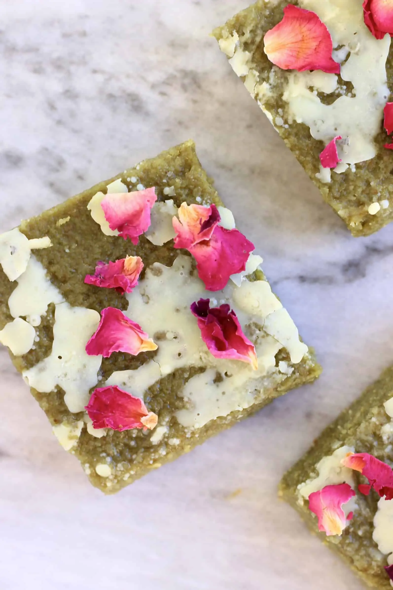 Three gluten-free vegan matcha brownies drizzled with white chocolate and decorated with rose petals