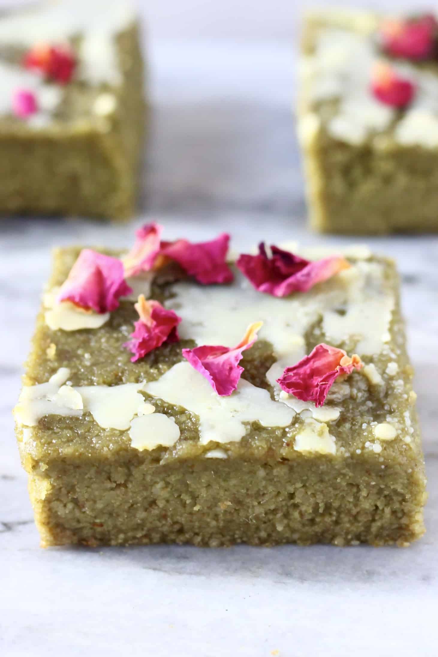 Three gluten-free vegan matcha brownies drizzled with white chocolate and decorated with rose petals