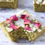 A gluten-free vegan matcha brownie topped with a white chocolate glaze and rose petals with a bite taken out of it