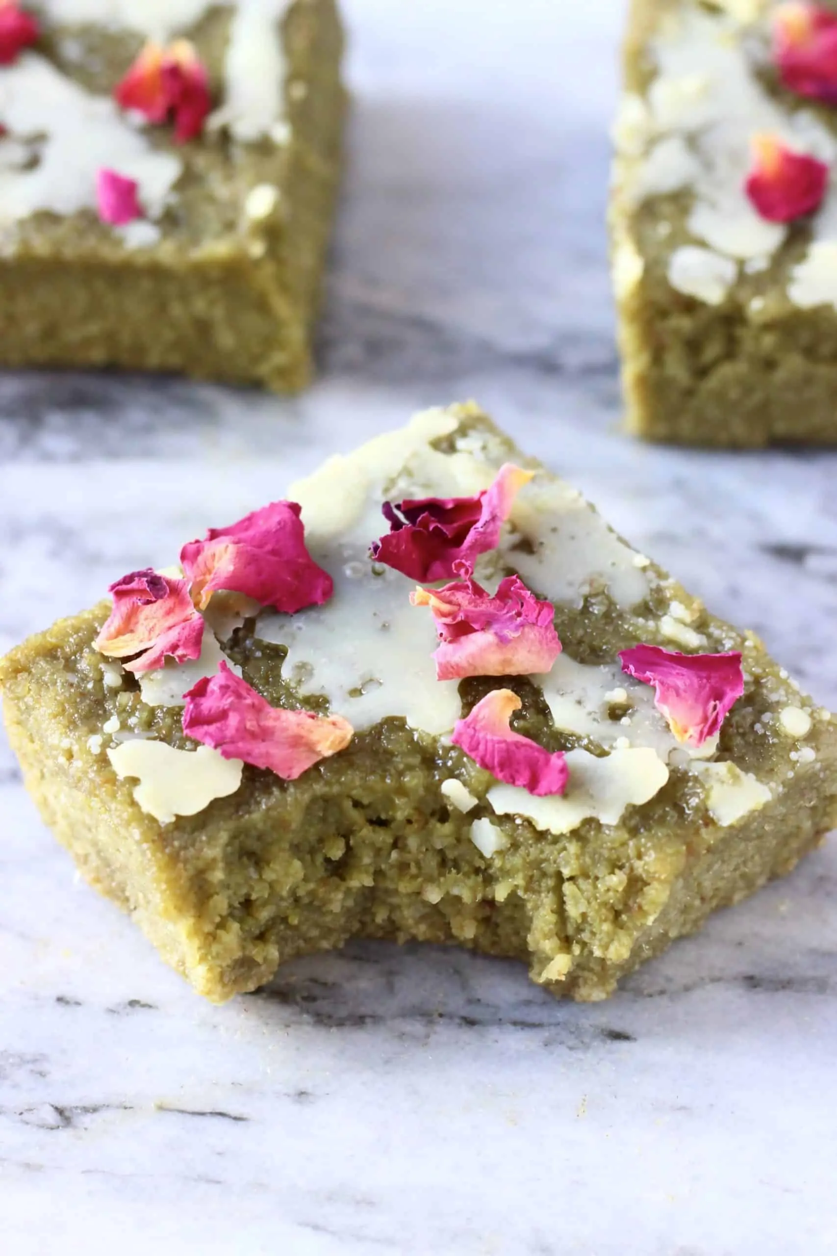 A gluten-free vegan matcha brownie topped with a white chocolate glaze and rose petals with a bite taken out of it