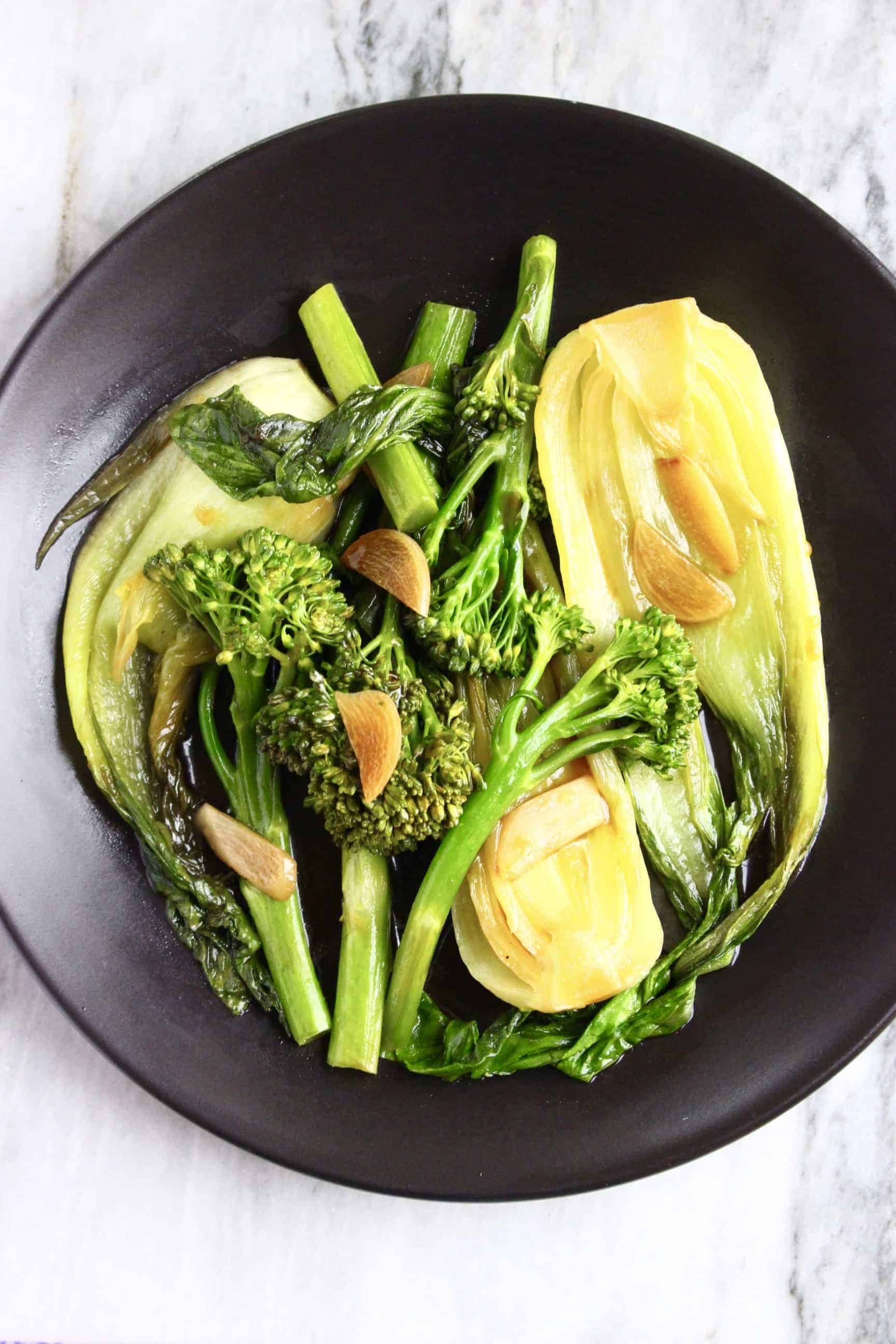 Wok-fried tenderstem broccoli, pak choi and sliced garlic on a black plate
