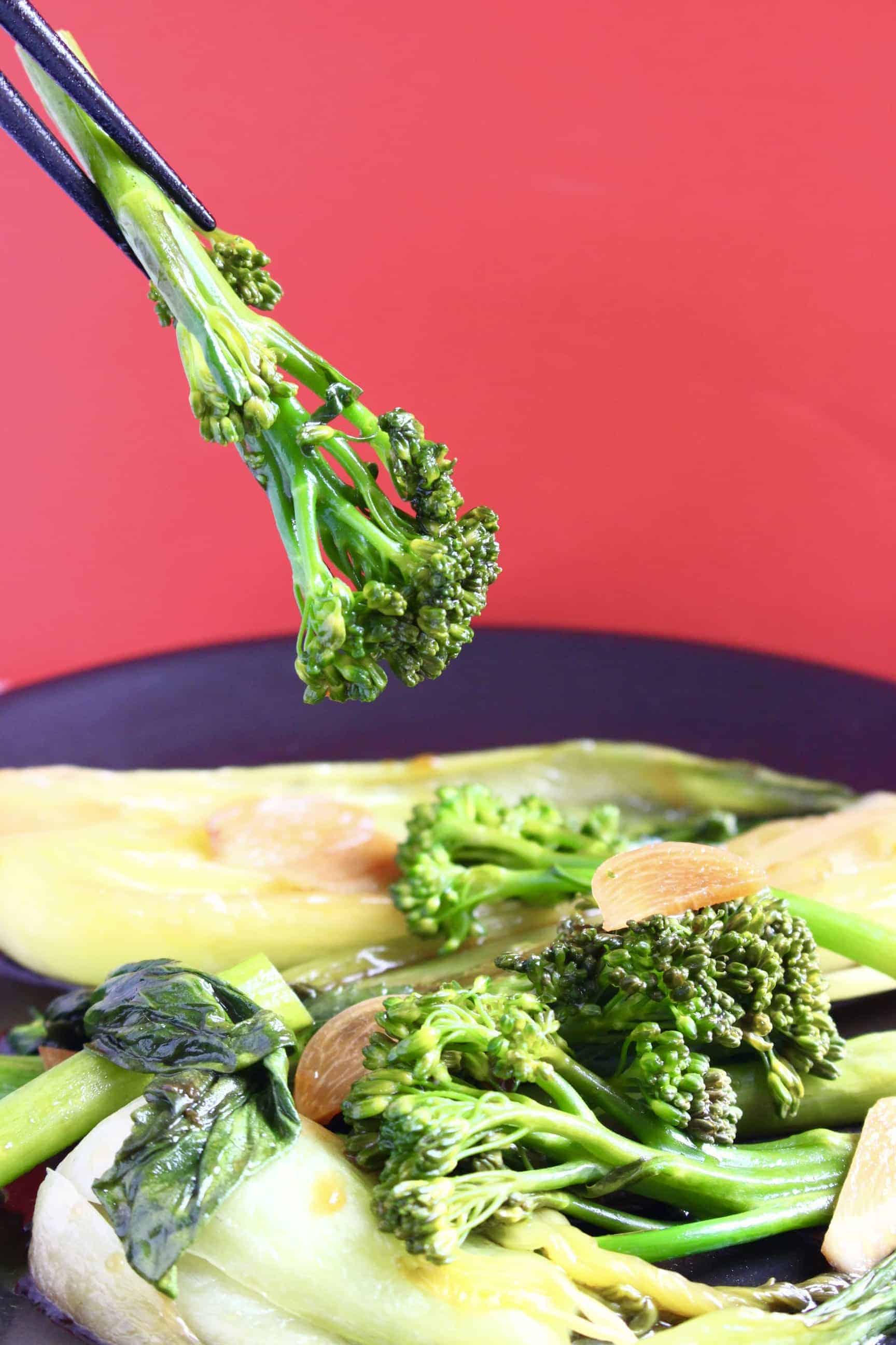 Wagamama wok-fried greens on a plate with a piece of tenderstem broccoli being lifted up with chopsticks 