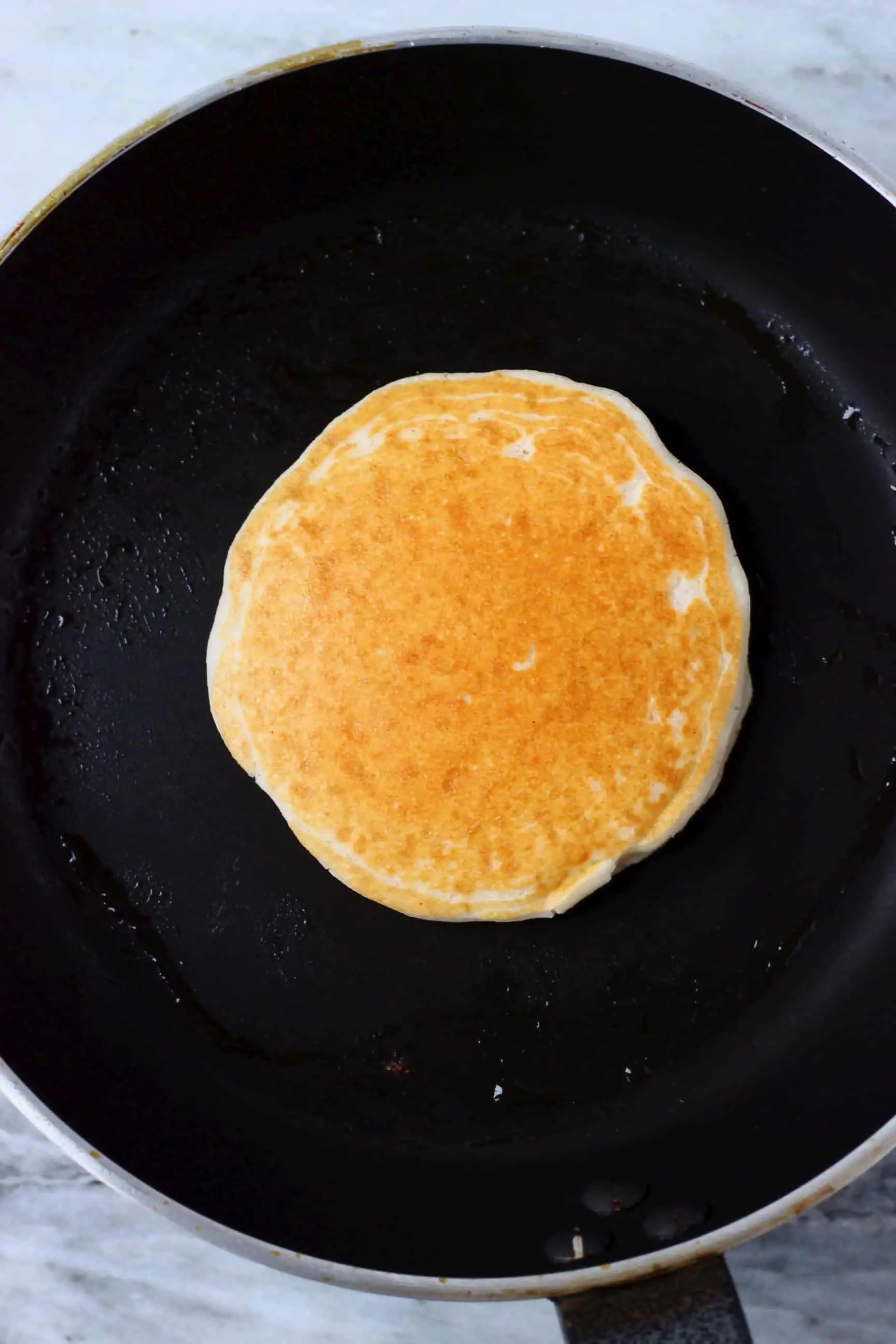 A golden brown gluten-free vegan pancake being cooked in a black frying pan 