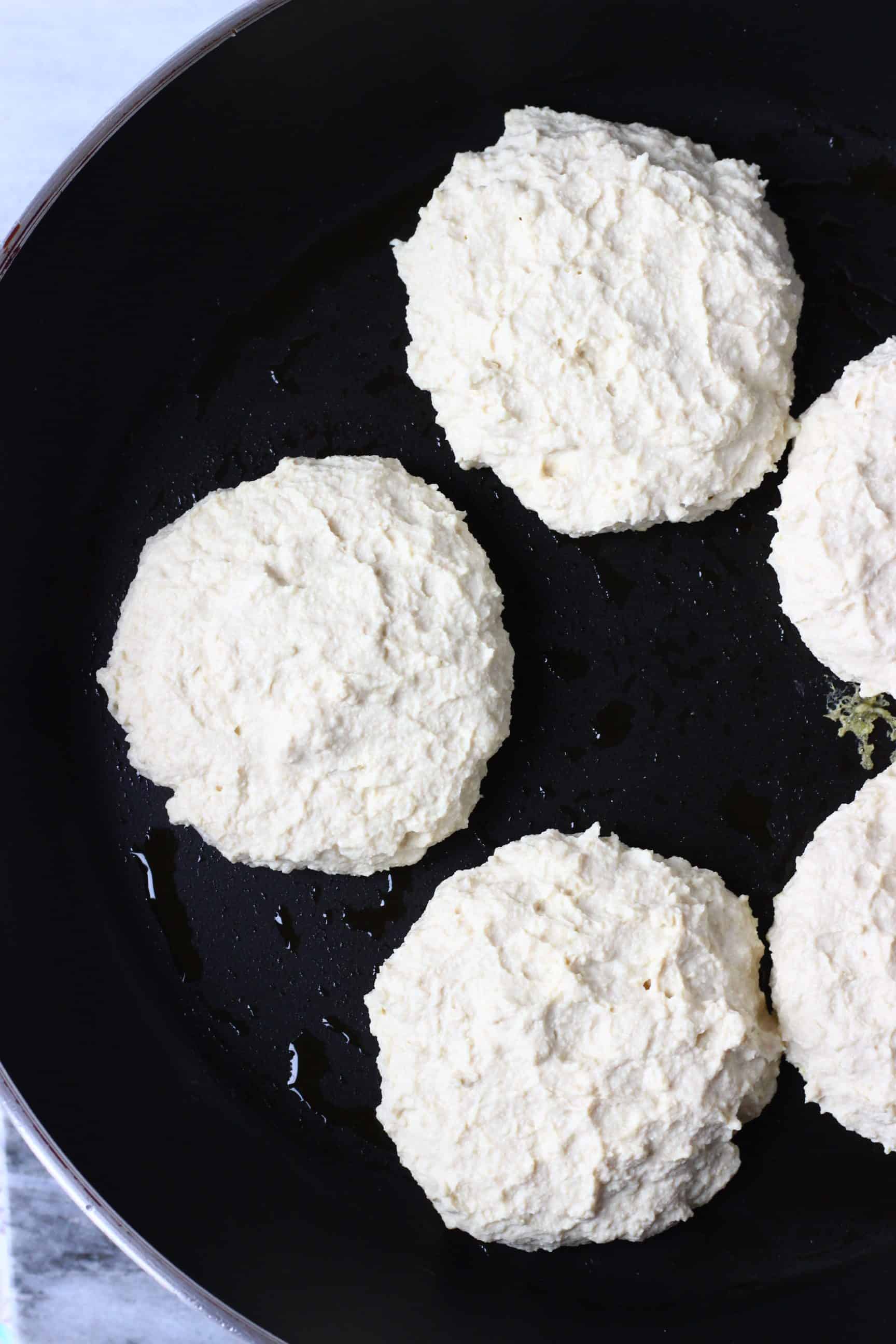 Five tofu burgers being fried in a black frying pan