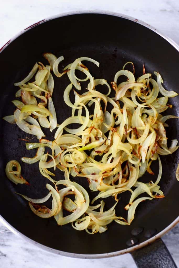 Sliced onions being fried in a black frying pan