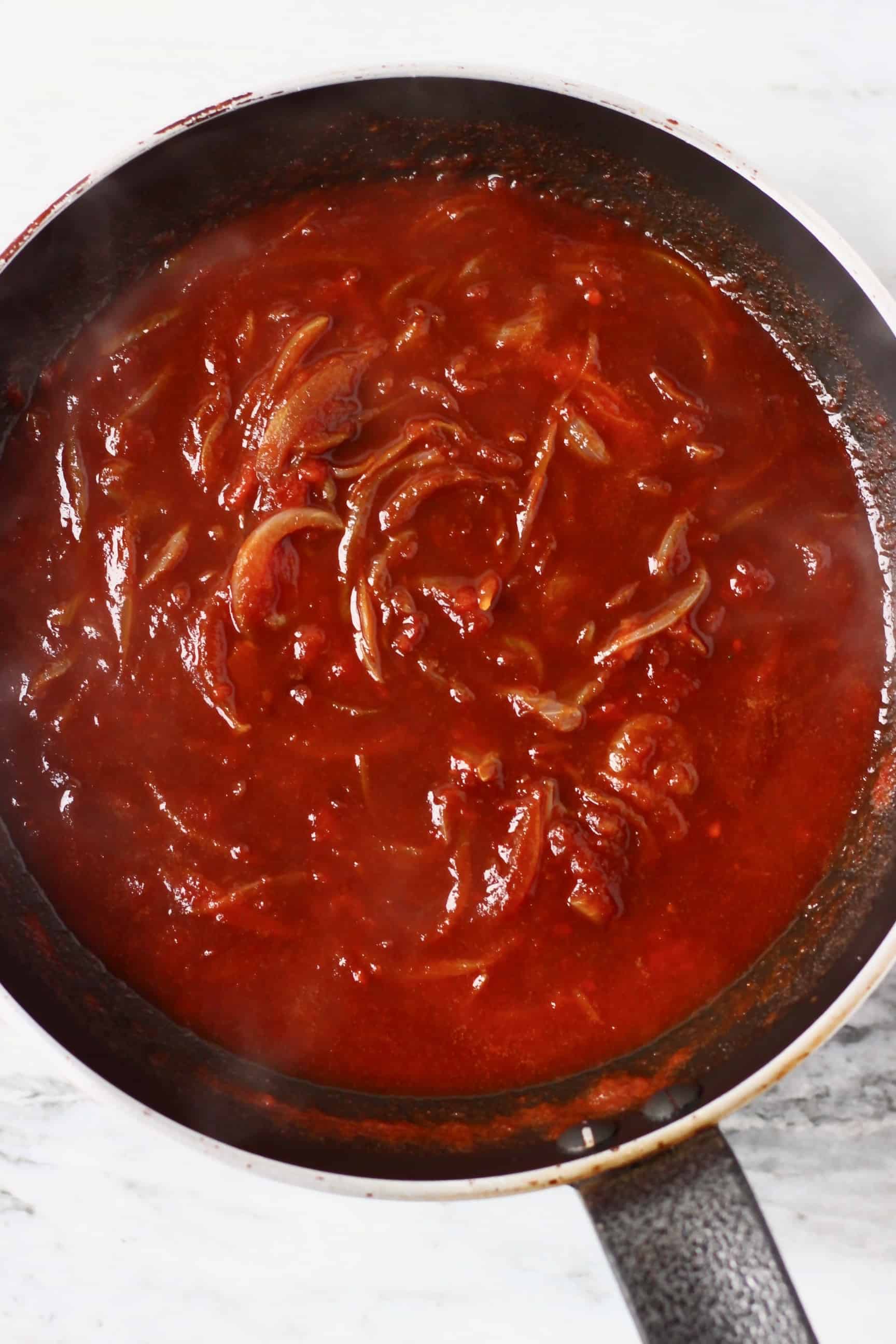 Onions with tomato sauce in a black frying pan against a marble background