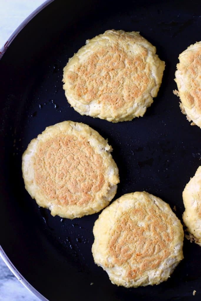 Five turned over tofu burgers being fried in a black frying pan