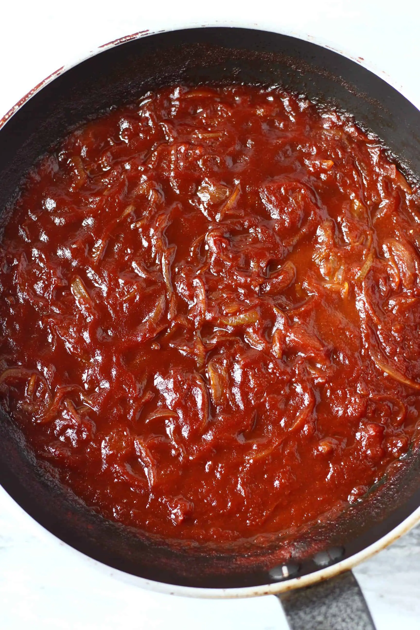Onions with tomato sauce in a black frying pan against a marble background