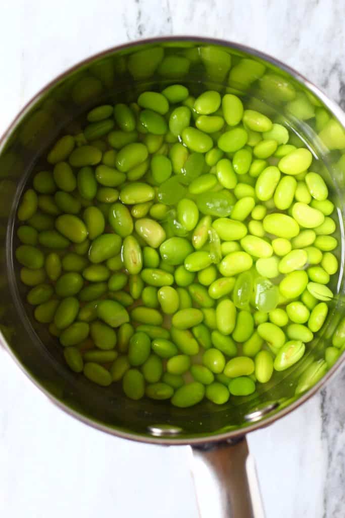 Edamame beans in water in a silver pan against a marble background