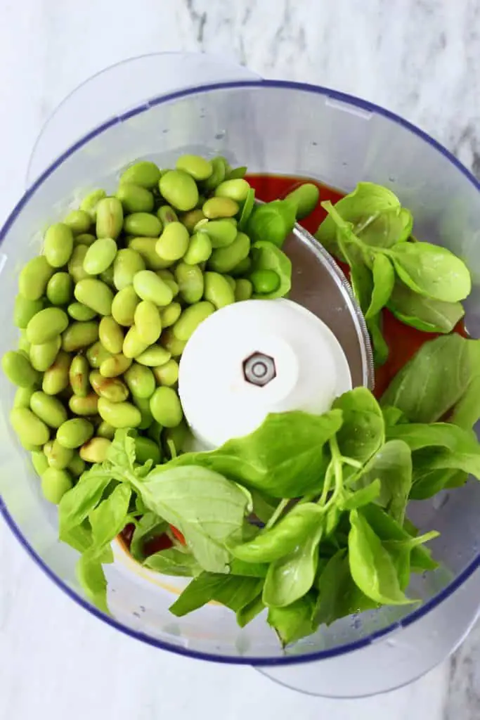 Edamame beans, basil and soy sauce in a food processor against a marble background