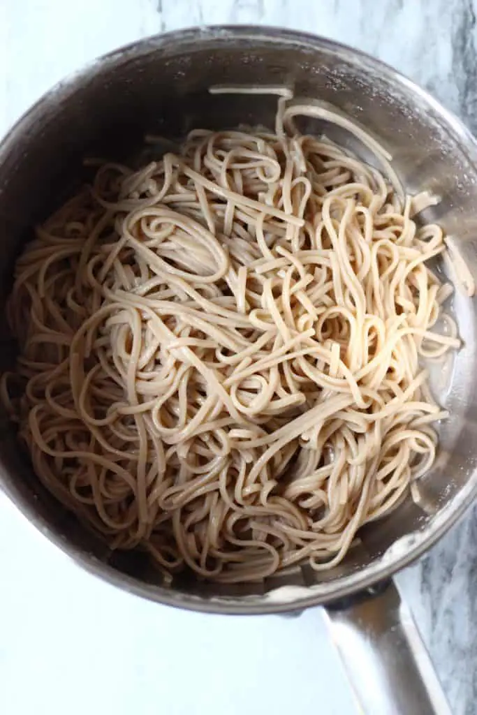 Cooked soba noodles in a silver pan against a marble background