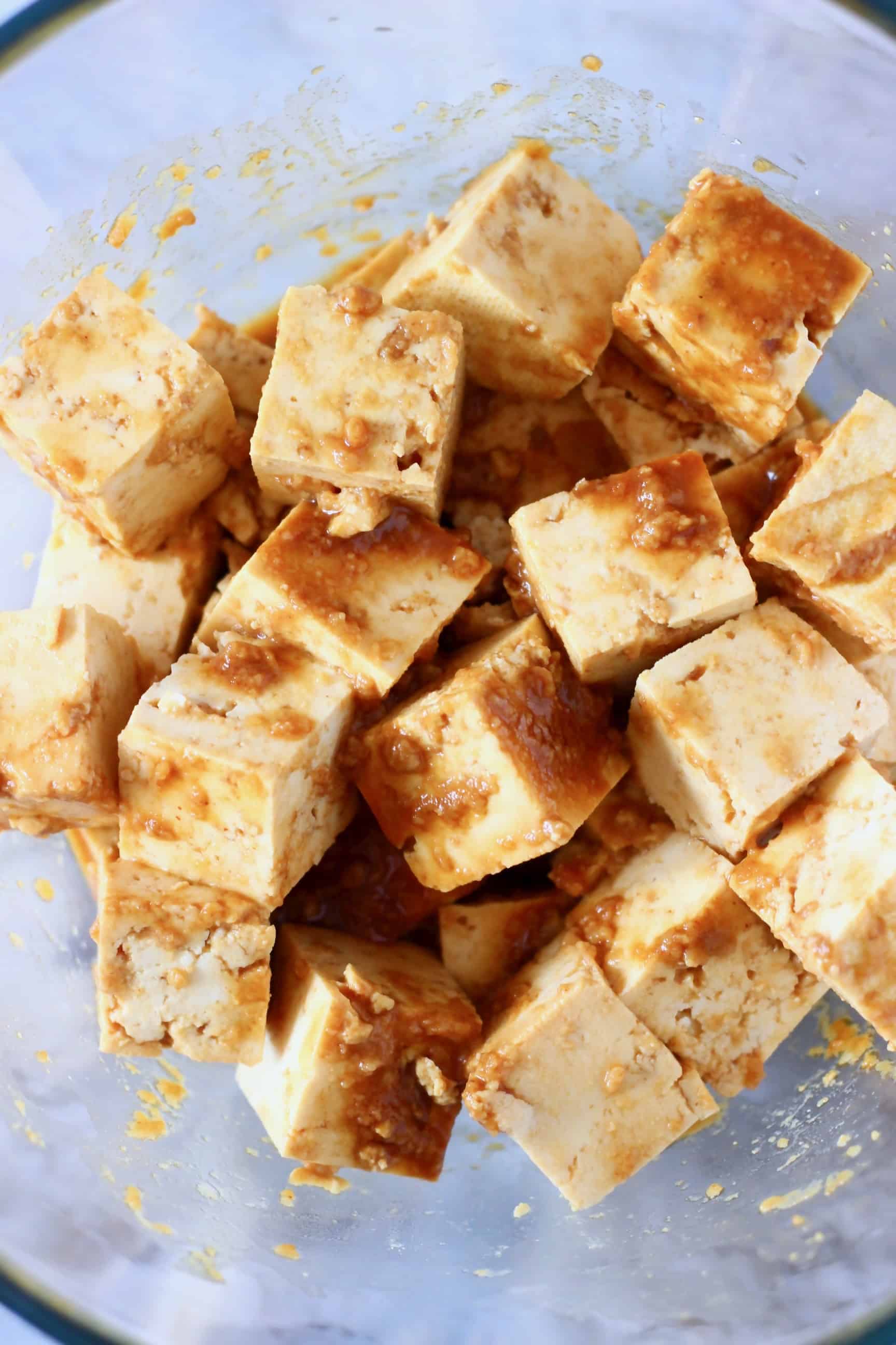 Cubes of tofu marinating in a peanut sauce in a glass bowl