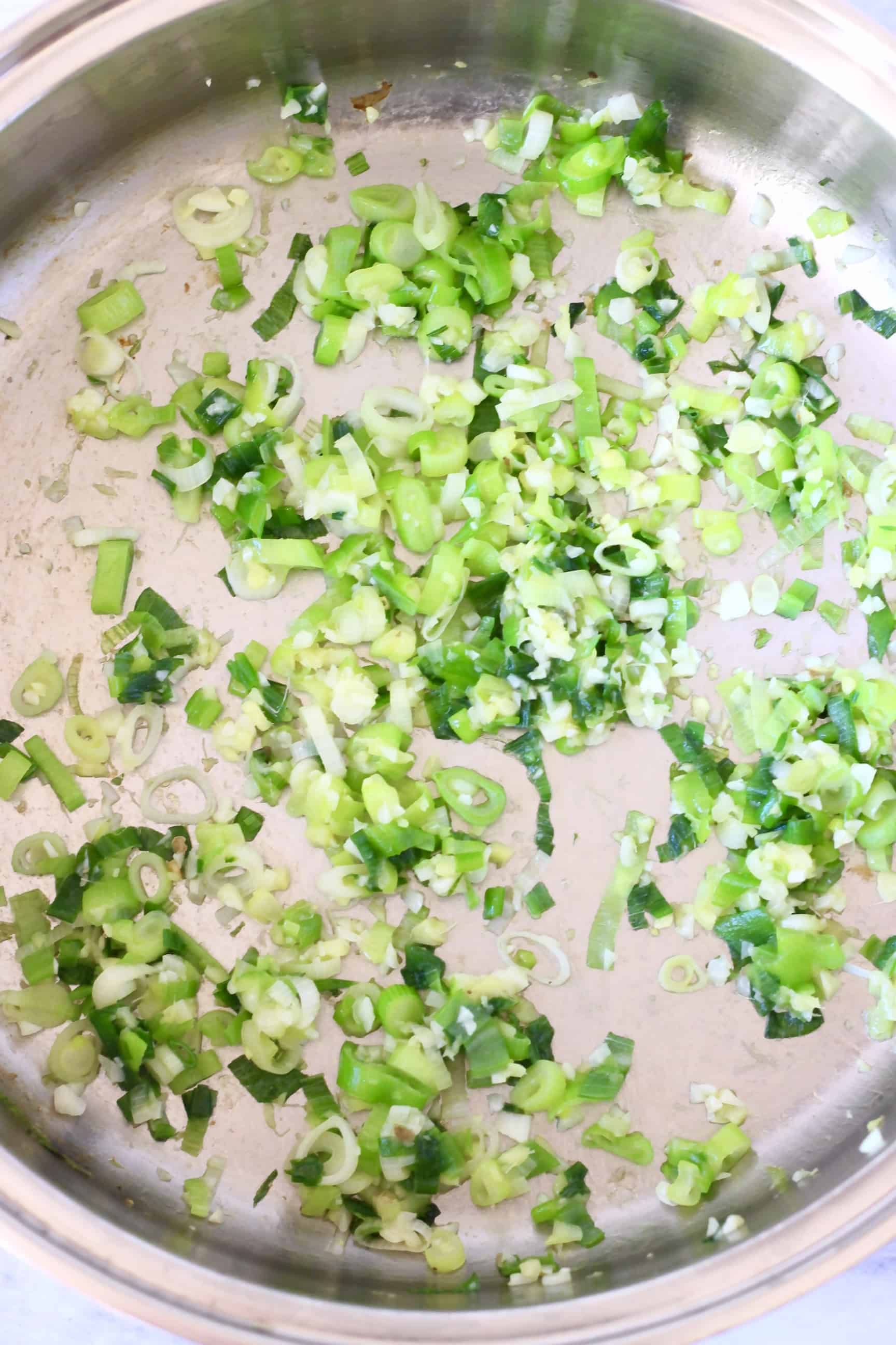 Sliced spring onions being fried in a silver pan