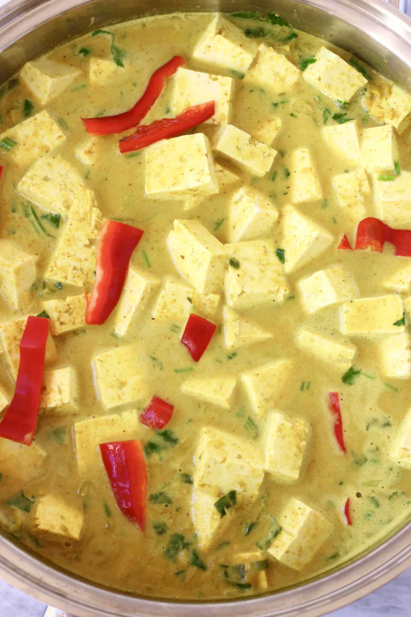 Cubes of tofu and strips of red pepper in a yellow curry sauce in a silver pan