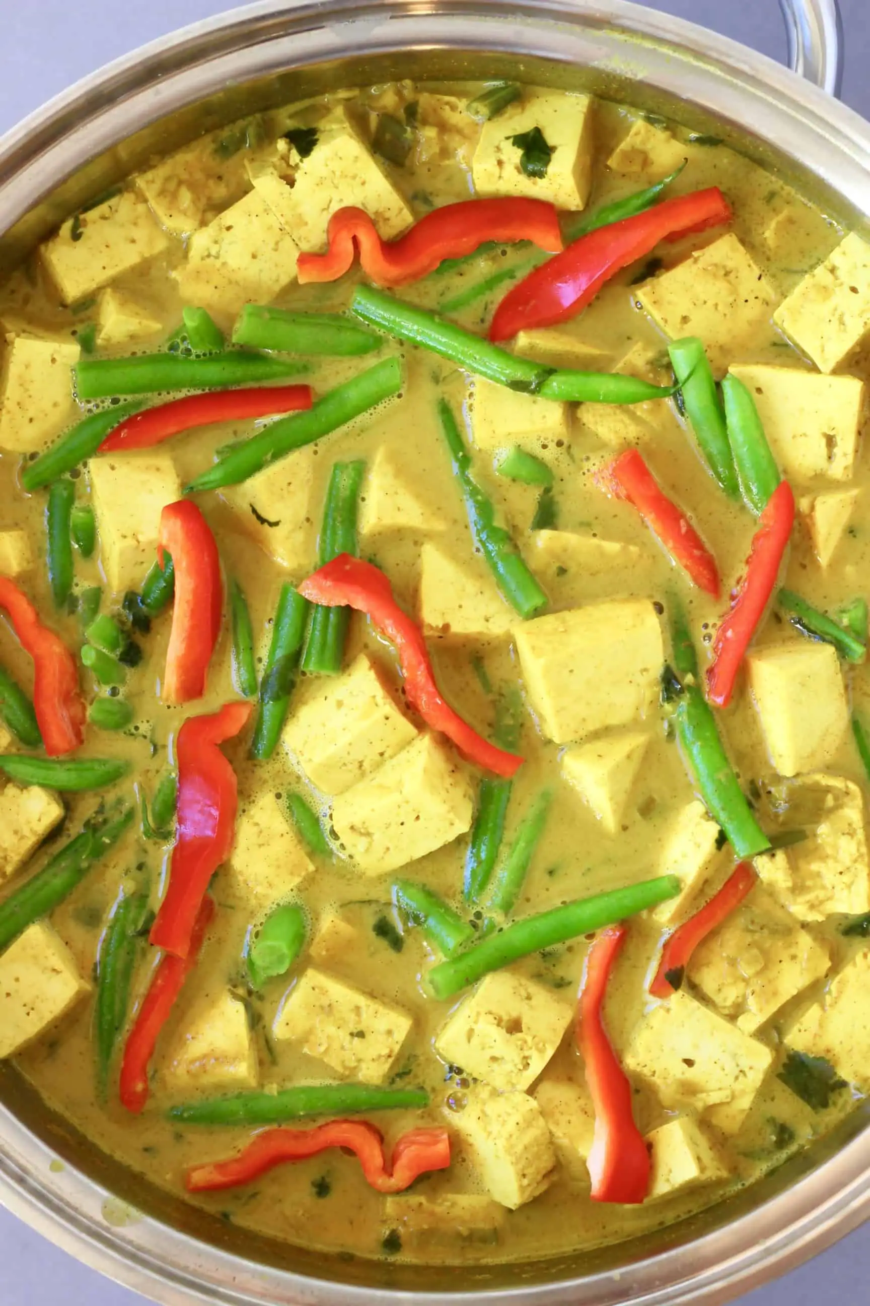 Cubes of tofu, green beans and strips of red pepper in a yellow curry sauce in a silver pan