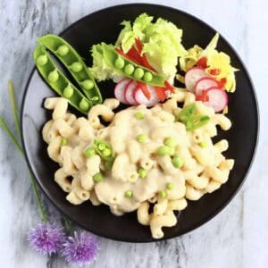 Vegan white bean mac and cheese with green peas on a black plate