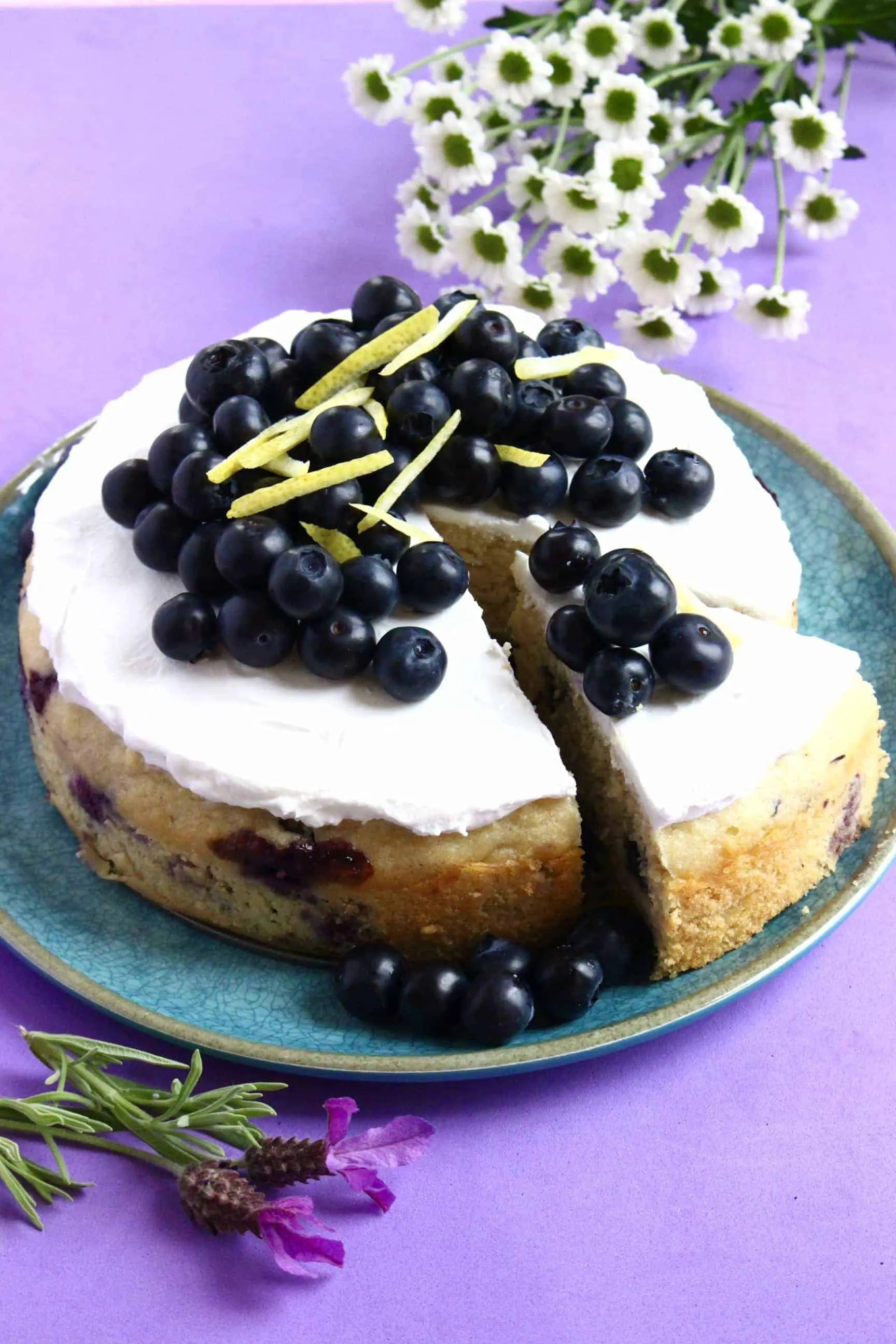Gluten-free vegan lemon blueberry cake topped with blueberries on a blue plate