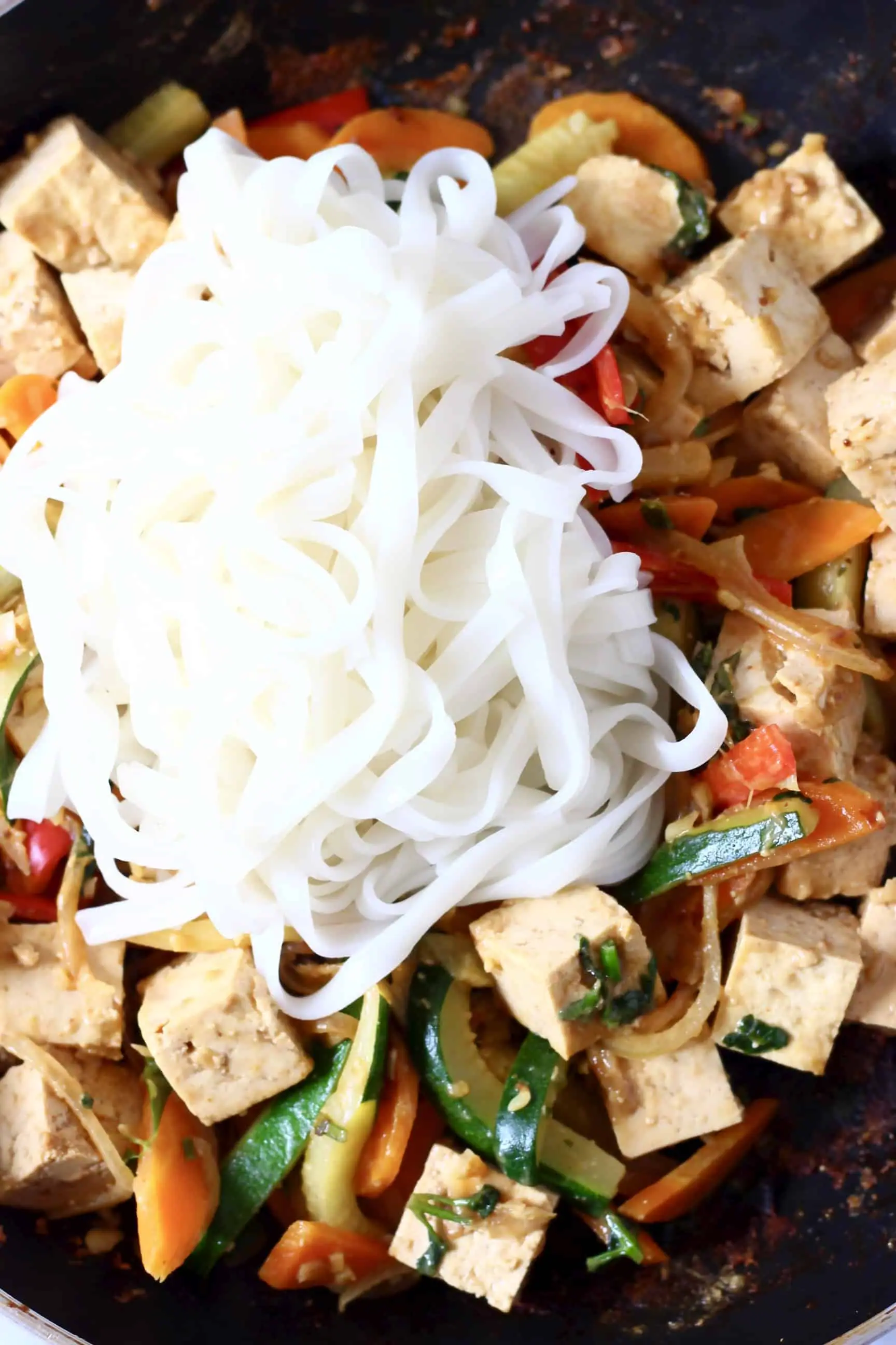 Chopped vegetables, tofu cubes and rice noodles in a frying pan