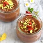 Two vegan chocolate pudding pots topped with chopped pistachios and freeze-dried raspberries