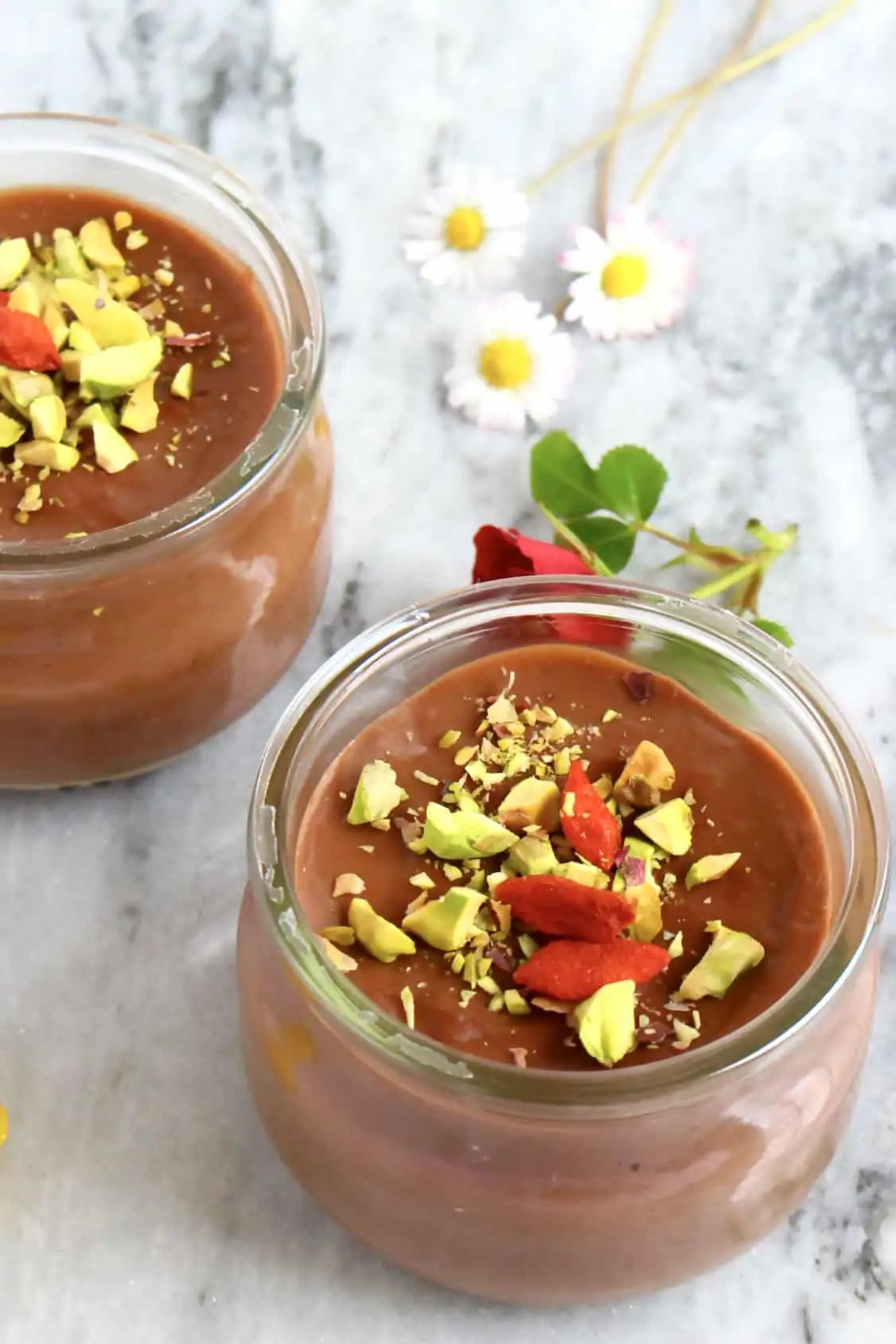 Two vegan chocolate pudding pots topped with chopped pistachios and freeze-dried raspberries