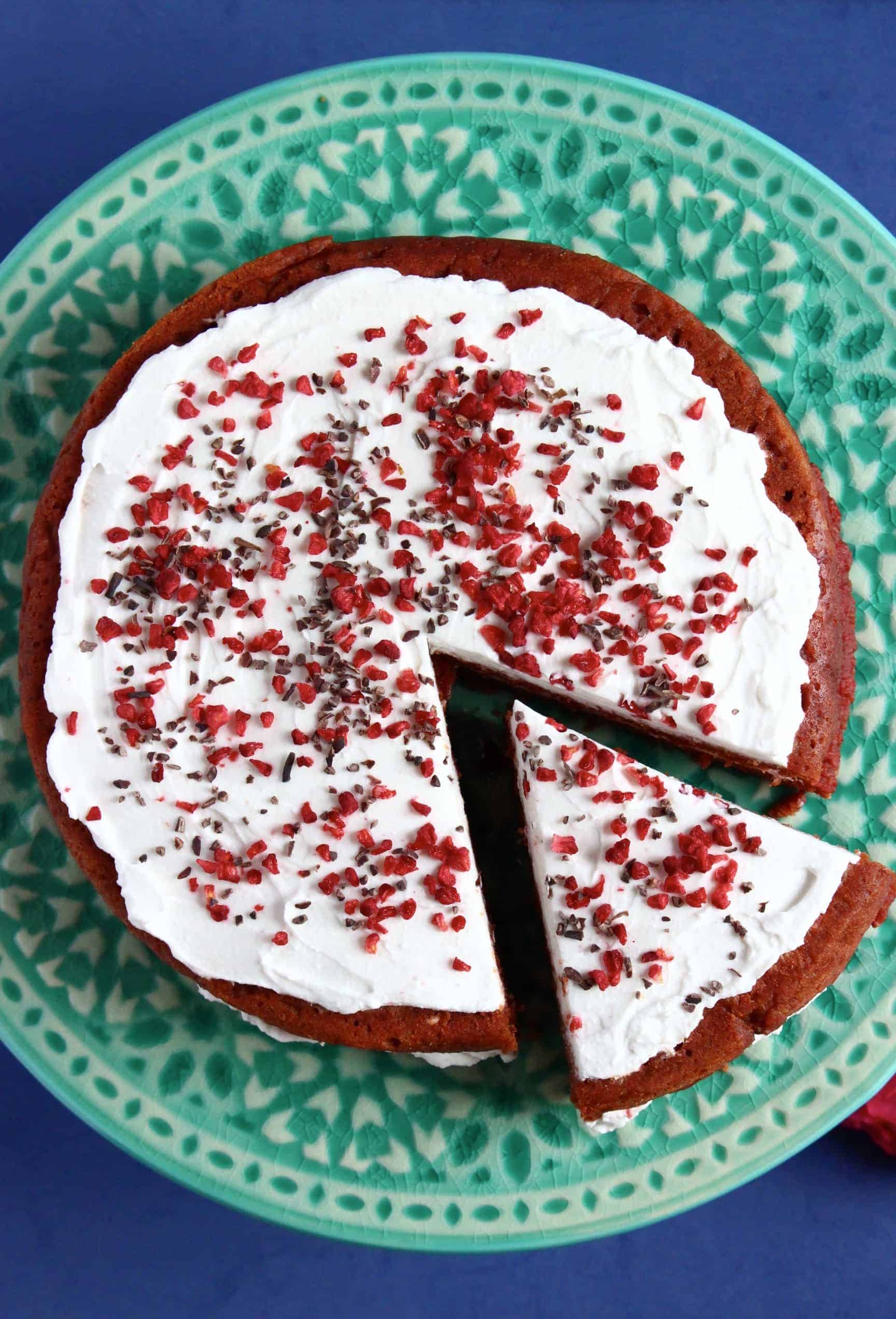 A gluten-free vegan red velvet cake topped on a cake stand with a slice taken out of it 