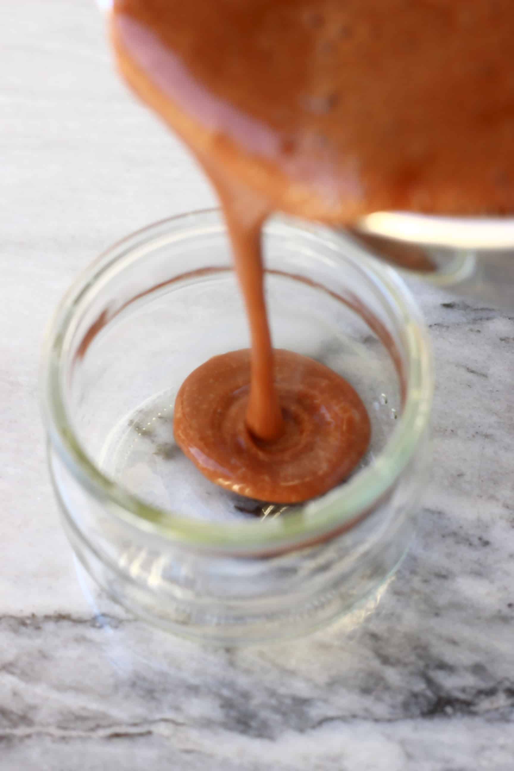 Vegan chocolate pudding mixture being poured into a glass pot from a pan