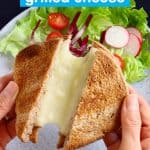 Grilled cheese sandwich being held up against a grey plate with salad on a black background