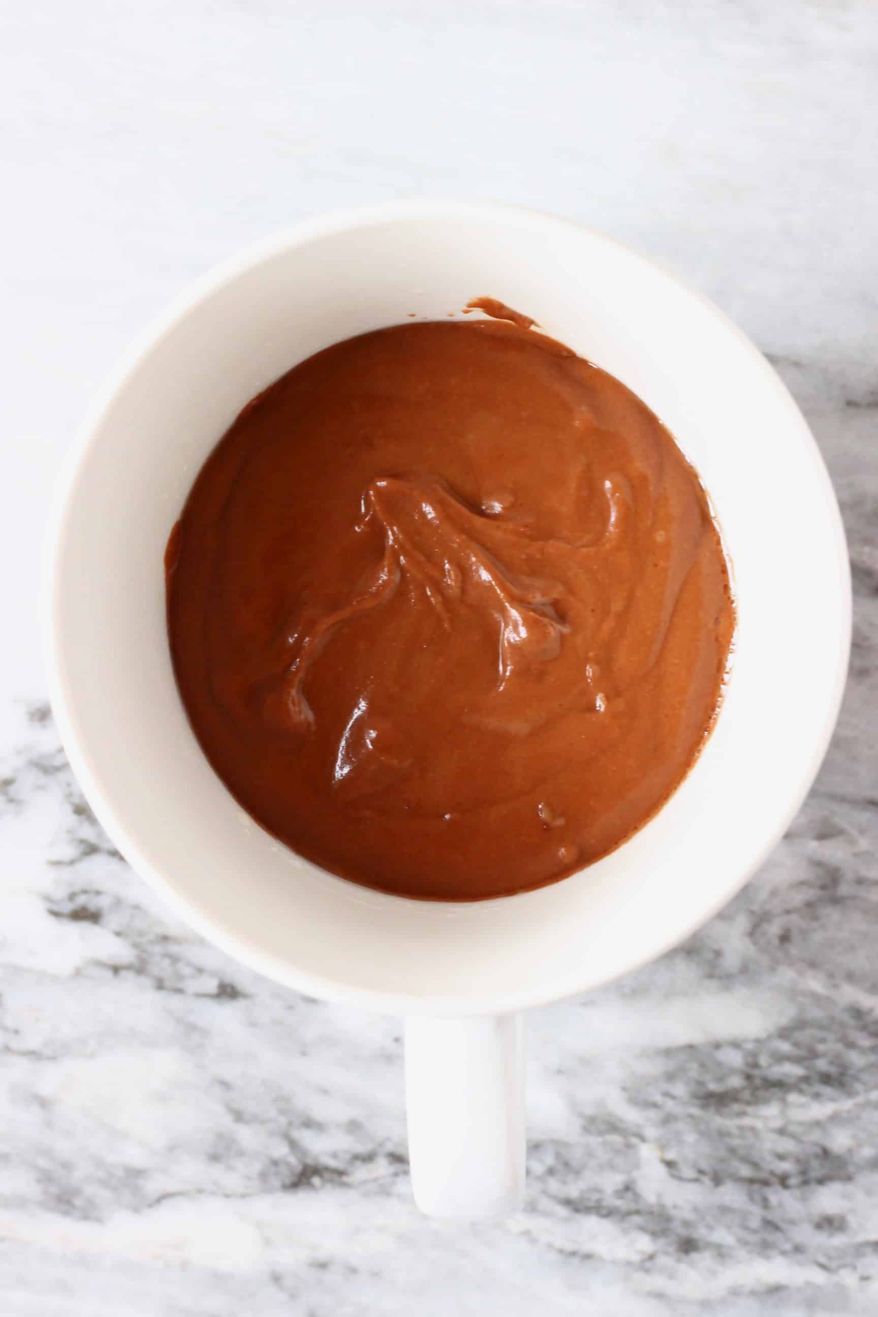 Vegan chocolate mug cake batter in a white mug against a marble background