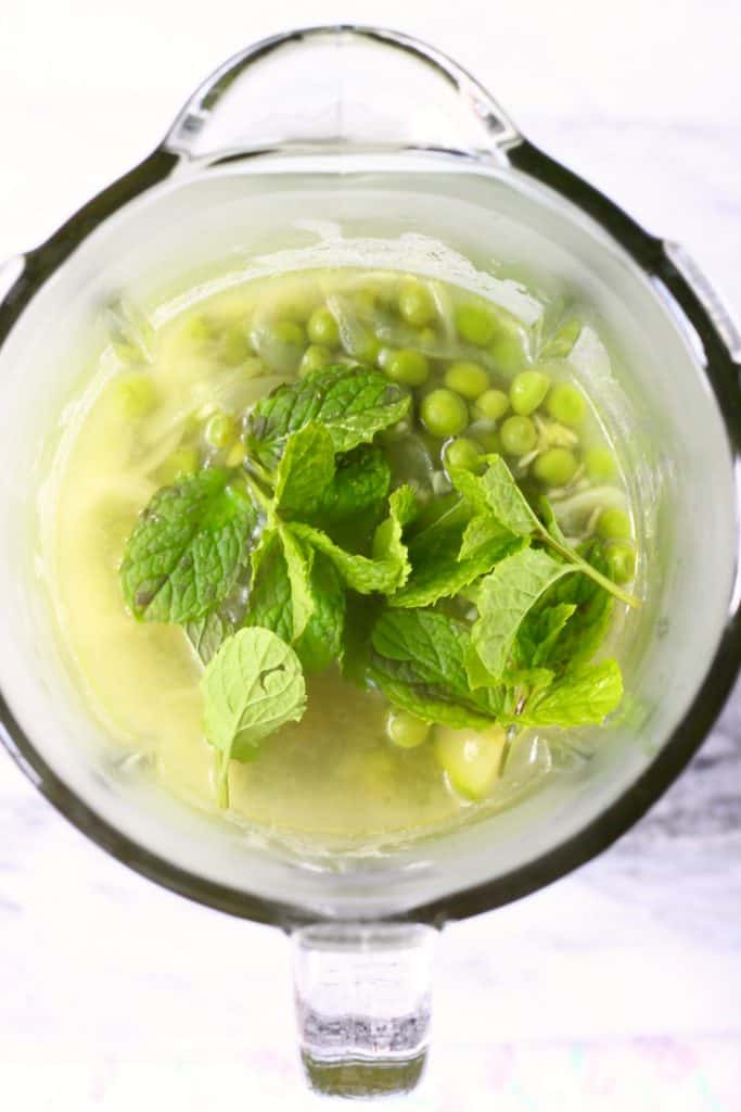 Zucchini, peas, fresh mint and water in a glass blender against a marble background