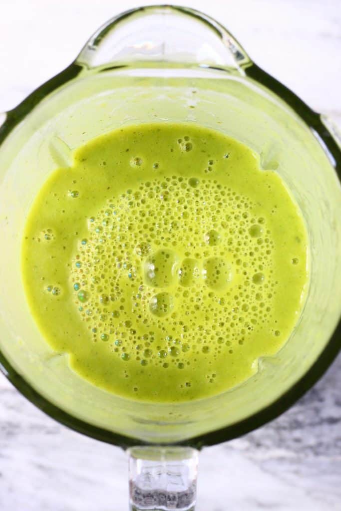 Green soup in a glass blender against a marble background