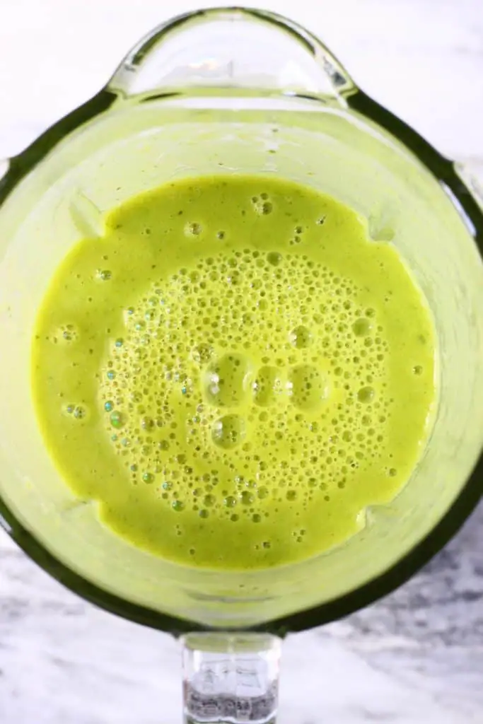 Green soup in a glass blender against a marble background