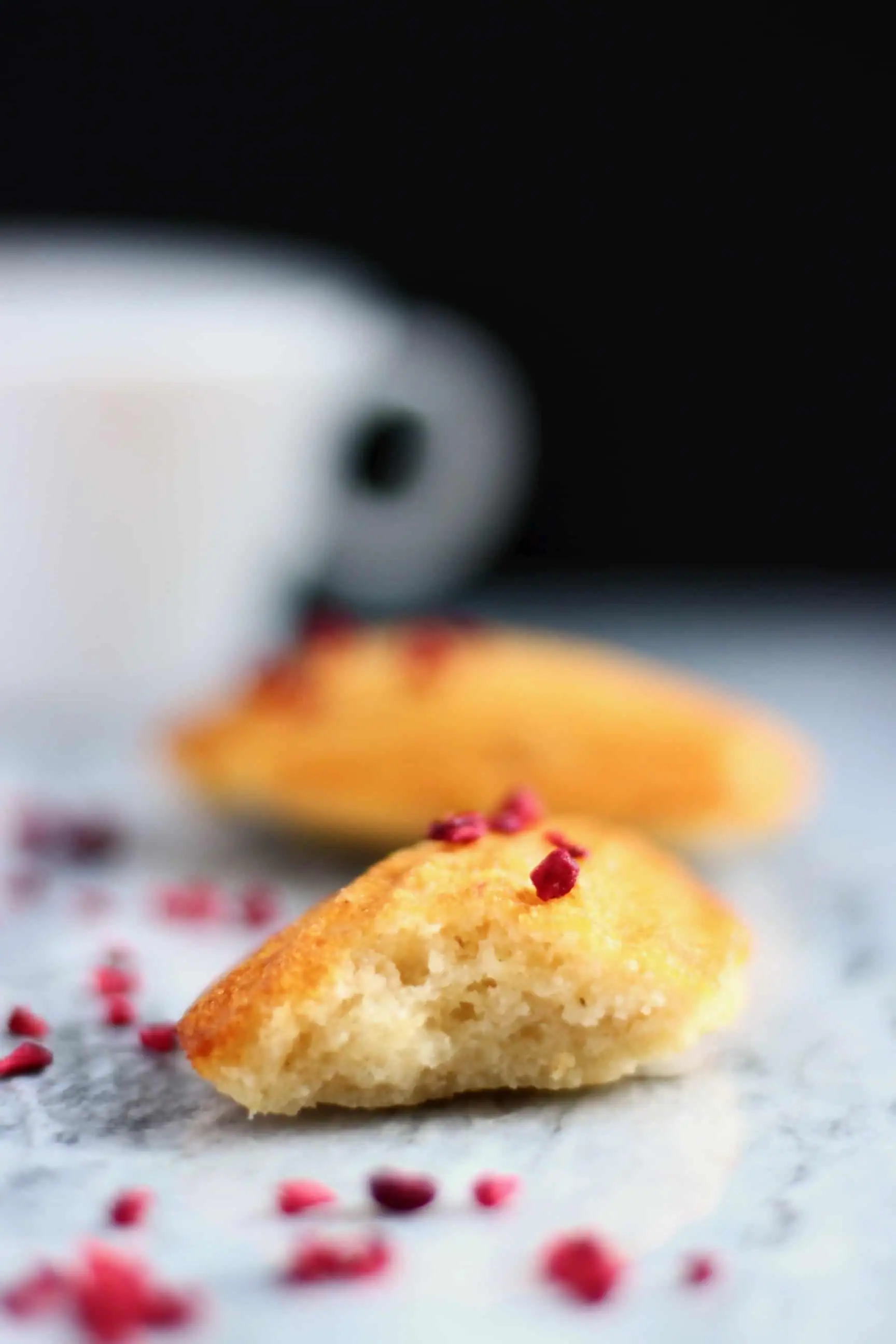 Two gluten-free vegan madeleines on a marble background with a white cup against a black background