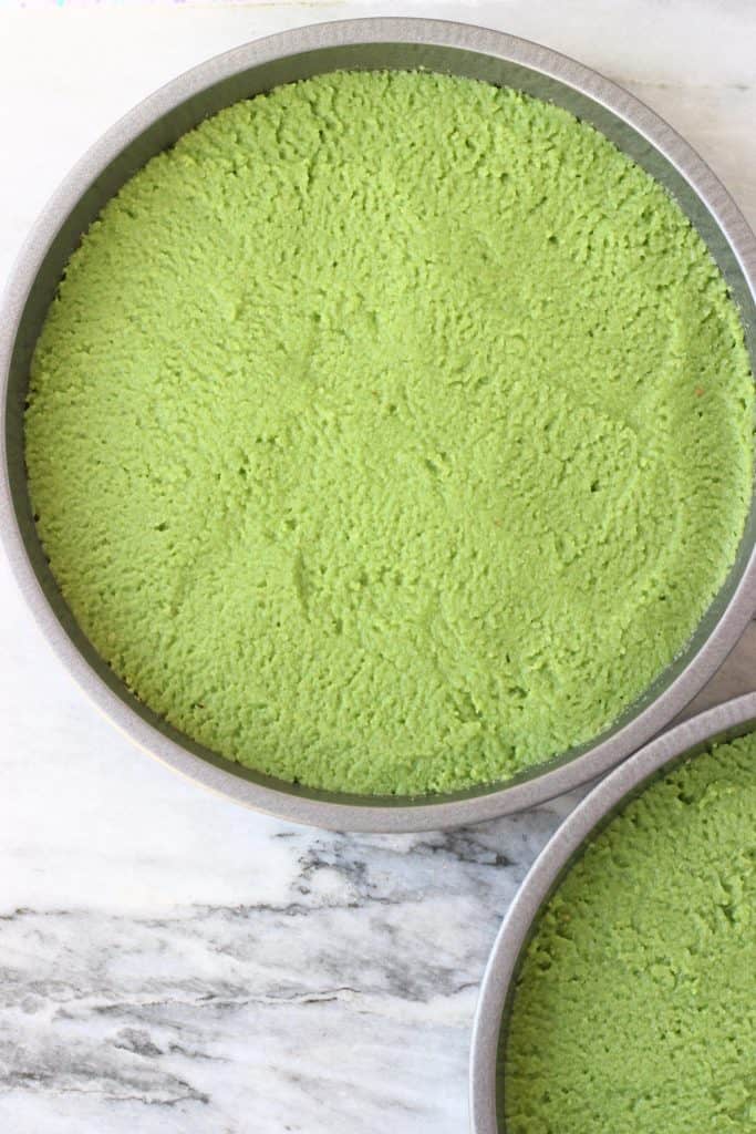 Raw matcha cake batter in two silver cake tin against a marble background