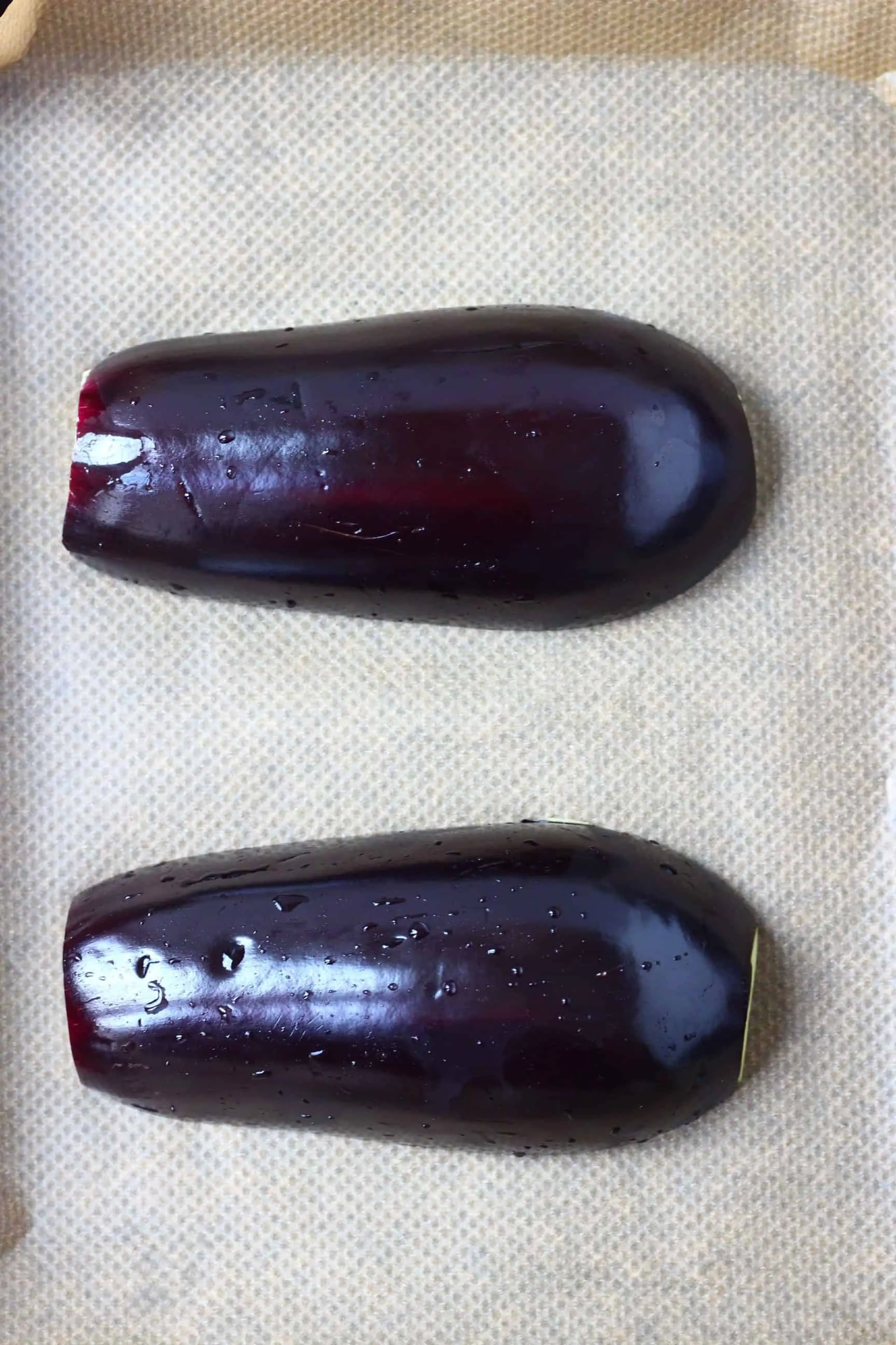 Two eggplant halves lying face down on a baking tray lined with baking paper