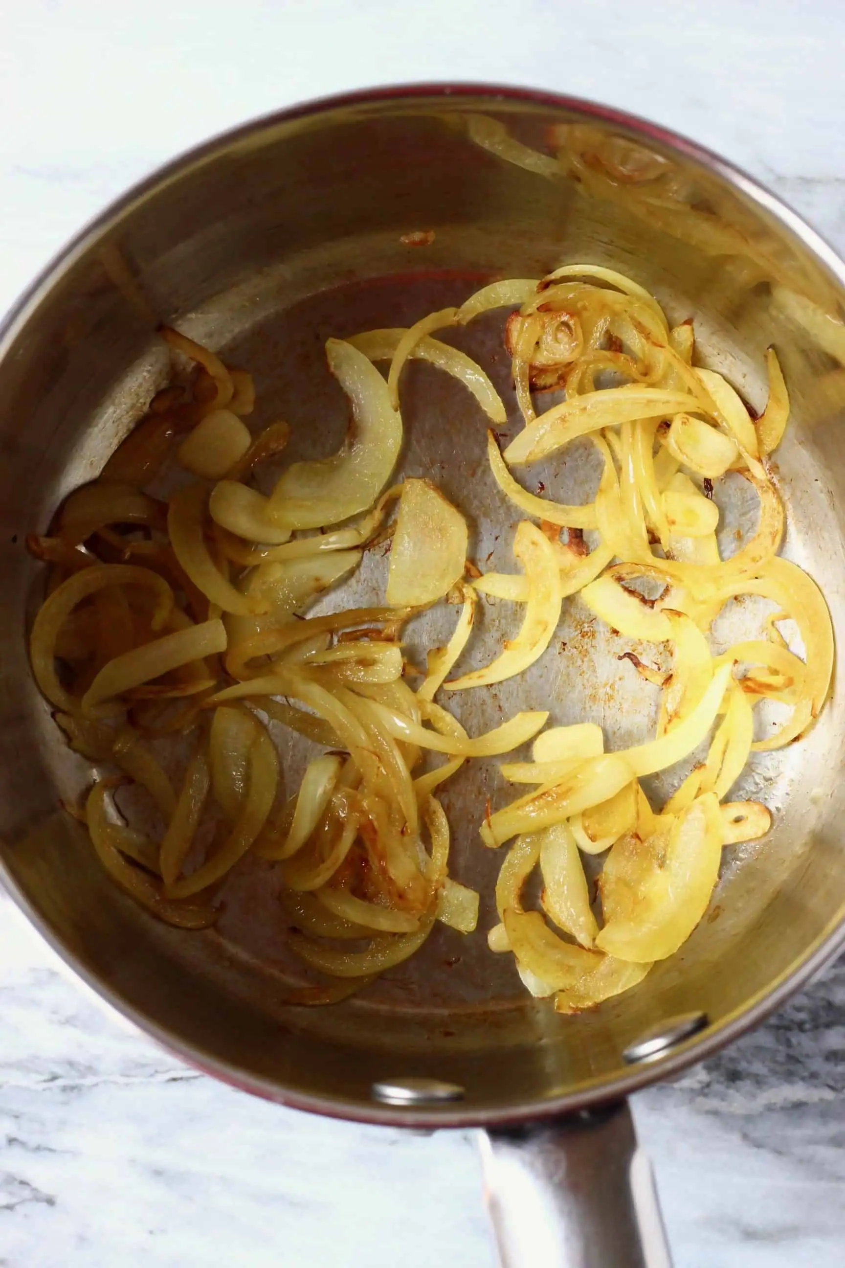 Sliced onion and garlic being fried in a silver saucepan