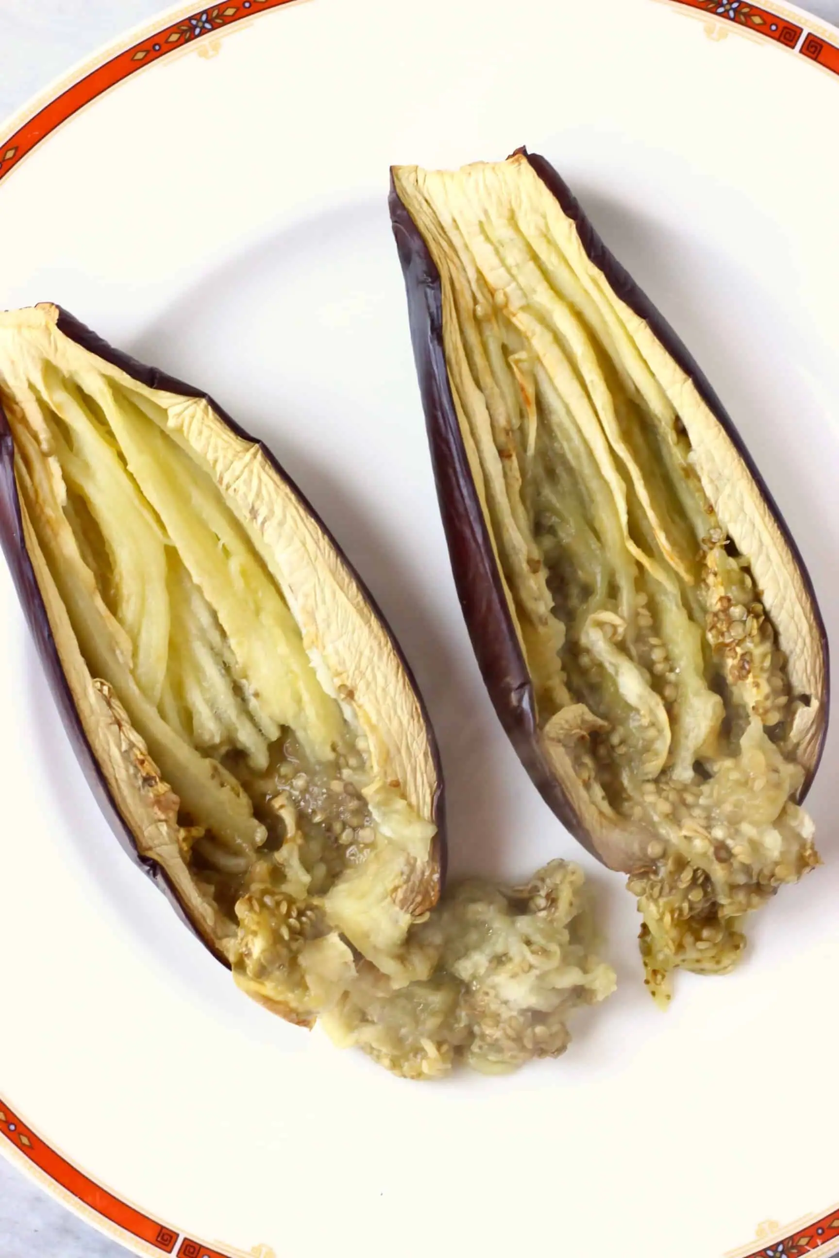 Two roasted eggplant halves being shredded on a white plate