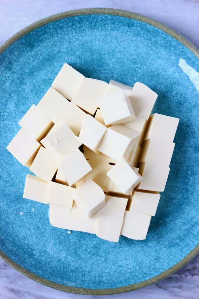 Tofu cubes on a blue plate against a marble background