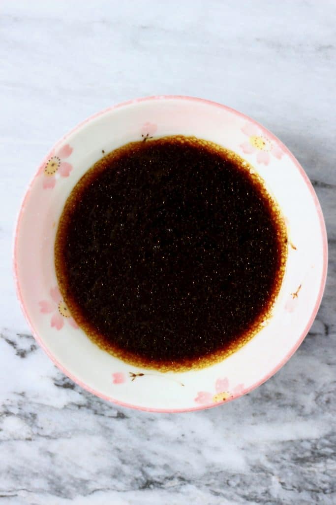 A light pink bowl filled with dark brown dressing against a marble background