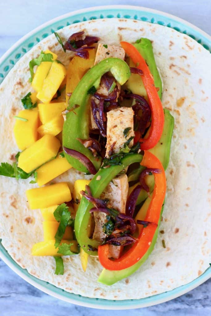 Photo of tofu, sliced peppers and diced mango on a tortilla on a blue plate